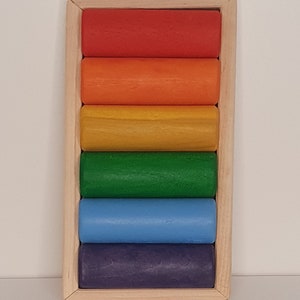 May include: A wooden rainbow stacking toy with six colorful cylinders in a wooden frame. The cylinders are red, orange, yellow, green, blue, and purple.