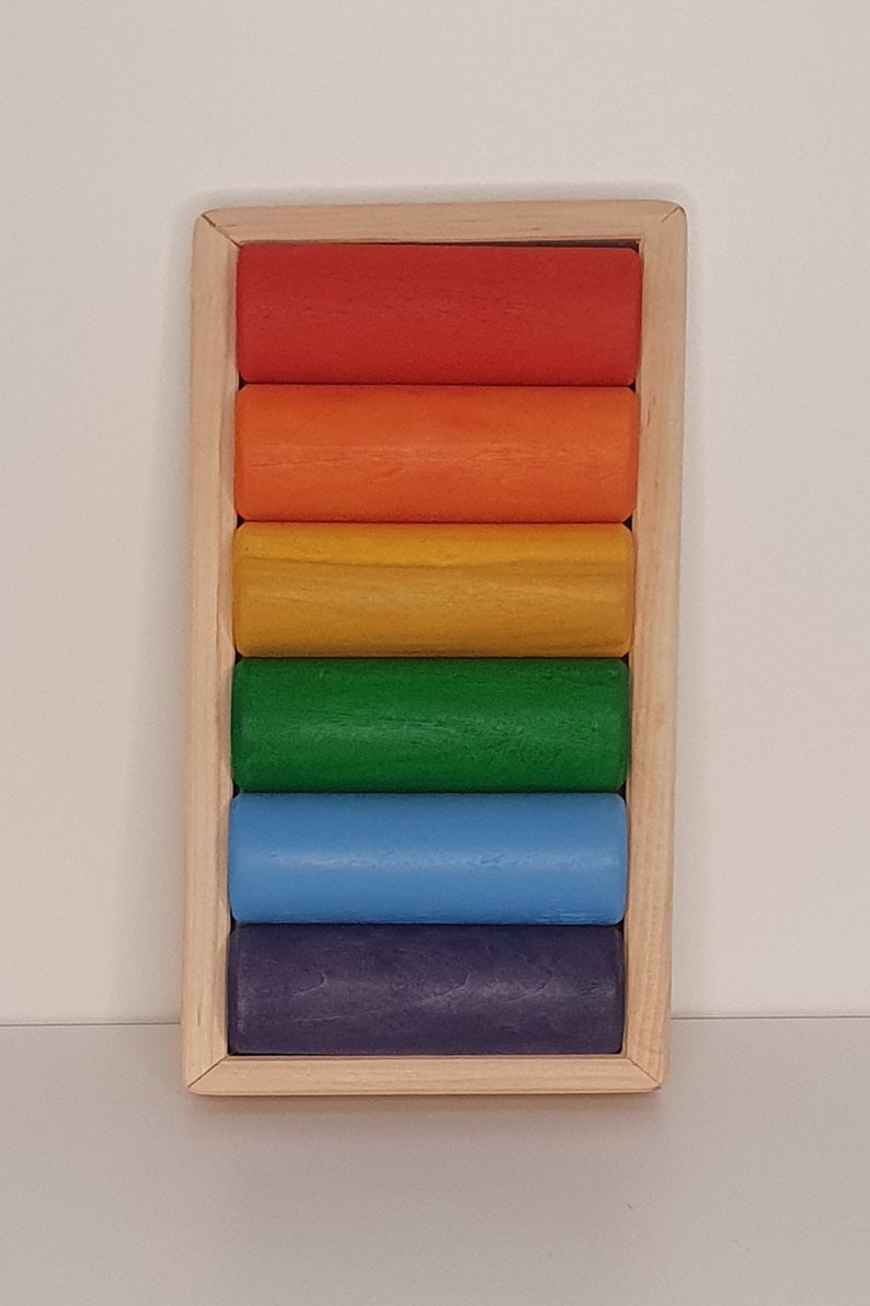 May include: A wooden rainbow stacking toy with six colorful cylinders in a wooden frame. The cylinders are red, orange, yellow, green, blue, and purple.