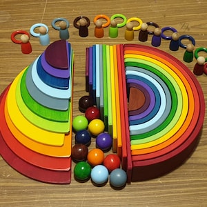 May include: A rainbow-colored wooden stacking toy with a set of colorful wooden people. The toy is made of 12 different colored rings that stack on top of each other. The rings are made of wood and have a smooth finish. The people are also made of wood and have painted faces. The toy is a great way for children to learn about colors and shapes.
