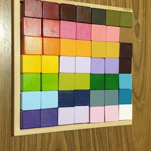 May include: A wooden educational toy featuring a grid of 64 colorful, square blocks in a rainbow of hues. The blocks are arranged in a wooden frame. Additional wooden toys are visible in the background.