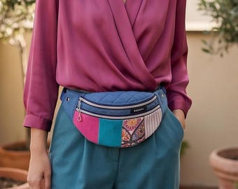 May include: A bum bag featuring a quilted blue denim upper section and a lower panel composed of vertical strips in magenta, teal, and a multi-coloured floral pattern. The bag includes a silver zip, a metal pull, and a black label with white text.