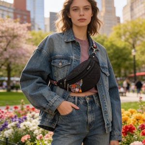 May include: A black quilted fanny pack with a zippered closure and a colorful patterned accent panel on the lower front. The bag features a multi-colored adjustable strap and a small rectangular label with the text T R I B E on the front.