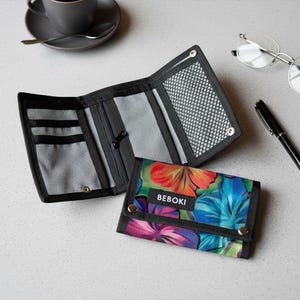 Puede incluir: Una cartera negra con estampado floral, abierta y cerrada, con un estampado floral a juego. La cartera abierta revela ranuras para tarjetas y un bolsillo de malla. La cartera cerrada tiene un vibrante estampado floral con el texto "BEBOKI".