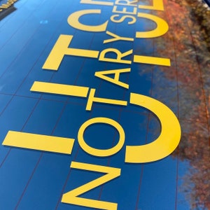 May include: A yellow vinyl sticker on a blue car window that says "Notary Services".