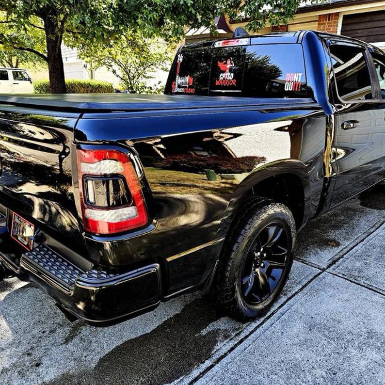 May include: Black pickup truck with a black tonneau cover. The truck has a "Don't Quit!" sticker on the back window and a "C.F.T.D Warrior" sticker on the rear passenger side window.