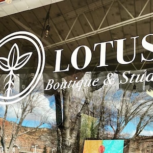 May include: A storefront window with a white sign that reads "LOTUS Boutique & Studio". The sign also features a white circle with a stylized plant inside.