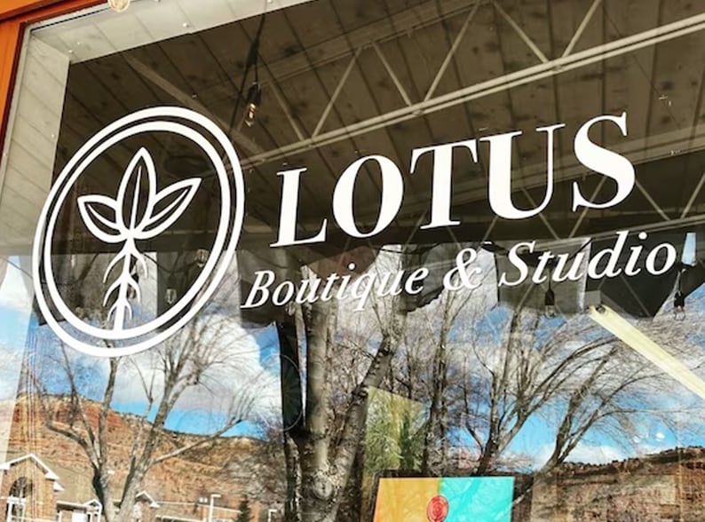 May include: A storefront window with a white sign that reads "LOTUS Boutique & Studio". The sign also features a white circle with a stylized plant inside.
