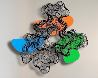 Könnte beinhalten: Abstrakte Metall-Wandkunst mit einem geschichteten, wellenförmigen Design in Schwarz, Orange, Grün und Blau. Das Kunstwerk ist an einer weißen Wand über einem grünen Sessel angebracht. Eine moderne Stehlampe mit drei kugelförmigen Lichtern steht daneben.