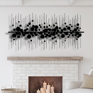 Puede incluir: Arte de pared de metal negro con líneas verticales y círculos, colgado sobre una chimenea de ladrillo blanco con velas en su interior. Un sillón blanco con un cojín a rayas se encuentra frente a la chimenea.