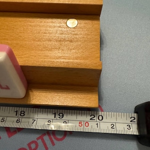 May include: Wooden game board with a light brown finish, featuring a recessed area and a small, round, gold-coloured accent. A measuring tape shows the board is approximately 50 cm long. Pink game pieces are visible.