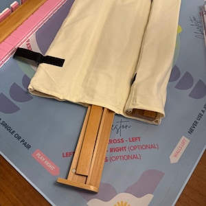 May include: A light blue game mat with text and illustrations, featuring a wooden rack and pink tiles. A beige cloth bag is secured with black straps. The game appears to be a version of Mahjong.