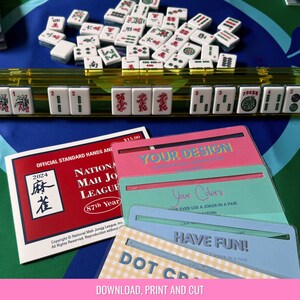 May include: A set of colorful printable cards with instructions to "Download, Print and Cut" for a game. The cards have a pink, blue, and yellow background with white text. The text on the cards includes "Your Design", "Your Colors", "Have Fun!" and "Dot Cards".
