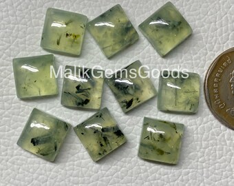 May include: Nine green gemstone cabochons with black inclusions, cut into square shapes. The stones are arranged in a random pattern on a white surface.