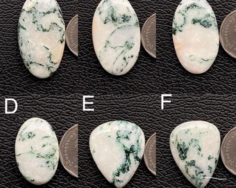Pode incluir: Seis pedras preciosas polidas com padrões brancos e verdes. As pedras têm formatos ovais e de gota. As pedras preciosas são exibidas em uma superfície preta. As pedras preciosas são provavelmente para fabricação de joias ou colecionismo.