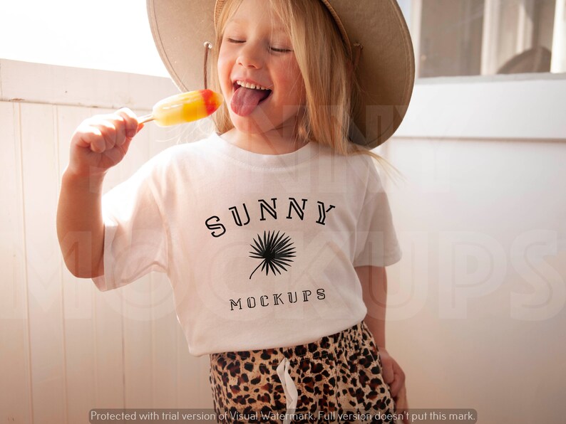May include: A young person wearing a white t-shirt with the text "SUNNY MOCKUPS" and a palm tree graphic. The person is wearing a straw hat and holding a popsicle.
