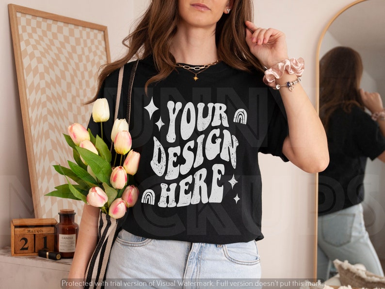 Puede incluir: Una camiseta negra con un gr&aacute;fico blanco que dice "YOUR DESIGN HERE" en una fuente retro. El gr&aacute;fico incluye estrellas e arco&iacute;ris.