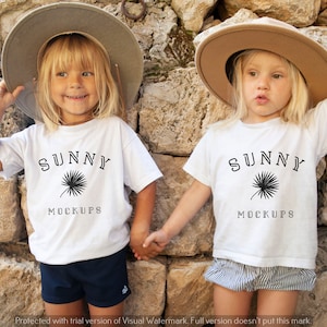 Puede incluir: Dos niños con camisetas blancas con el texto "SUNNY MOCKUPS" y un gráfico de palmera. Las niñas llevan sombreros de paja y se toman de la mano.