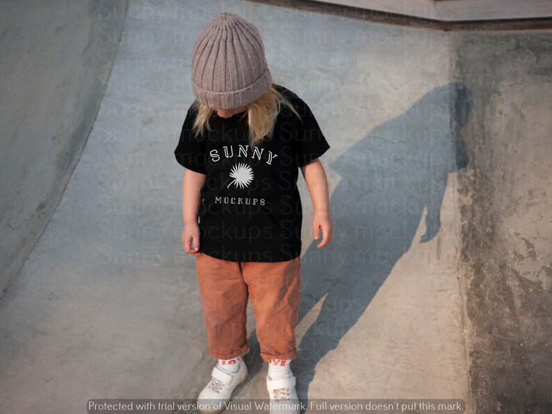 Puede incluir: Un ni&ntilde;o con una camiseta negra con un gr&aacute;fico blanco de una palmera y el texto "SUNNY MOCKUPS". El ni&ntilde;o tambi&eacute;n lleva una boina gris y pantalones marrones.