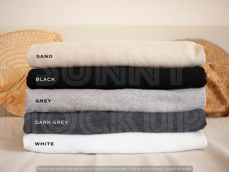 May include: A stack of five folded t-shirts in different colors: sand, black, grey, dark grey, and white. The shirts are folded neatly and stacked on top of each other.