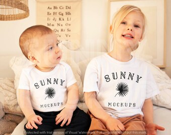 Puede incluir: Dos niños con camisetas blancas con un gráfico de palmera negra y el texto "SUNNY MOCKUPS". Los niños están sentados en una manta blanca y marrón.