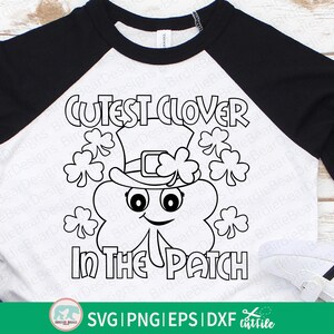 Pu&ograve; includere: Una maglietta bianca e nera in stile raglan con un design per la festa di San Patrizio. La grafica include un trifoglio sorridente con un cappello da folletto, circondato da trifogli, e la scritta "Cutest Clover in the Patch."