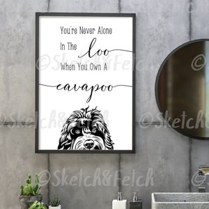May include: A black and white illustration of a cavapoo dog's head peeking out from the bottom of a white framed print. The print has the text "You're Never Alone In The loo When You Own A cavapoo" on it.