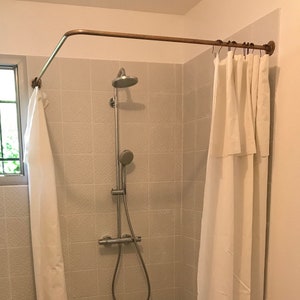 Può includere: Una tenda da doccia bianca con un'asta da doccia in rame e un soffione doccia argentato in un bagno piastrellato.