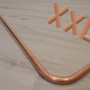 Könnte beinhalten: Eine Duschstange aus Kupfer mit einem 90-Grad-Knick. Die Stange ist mit einer Flansch an der Wand befestigt. Die Stange ist etwa 1,8 Meter lang. Die Stange befindet sich in einem Badezimmer mit einem weißen Fliesenboden.