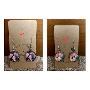 May include: Two pairs of earrings with silver hooks and round glass charms featuring a photo of the Golden Girls. The charms are labeled #1 and #2.