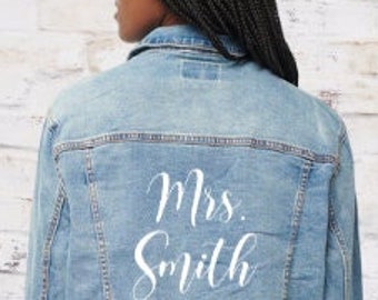 May include: A light blue denim jacket with the text "Mrs. Smith" in white script on the back.