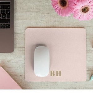 May include: A pink mouse mat with the initials "BH" in gold lettering. A white computer mouse is on the mat.
