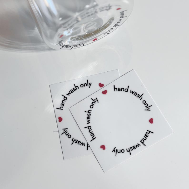 May include: Four white square stickers with the text "hand wash only" written in black around the edge of each sticker.  Each sticker has four small red hearts around the edge.