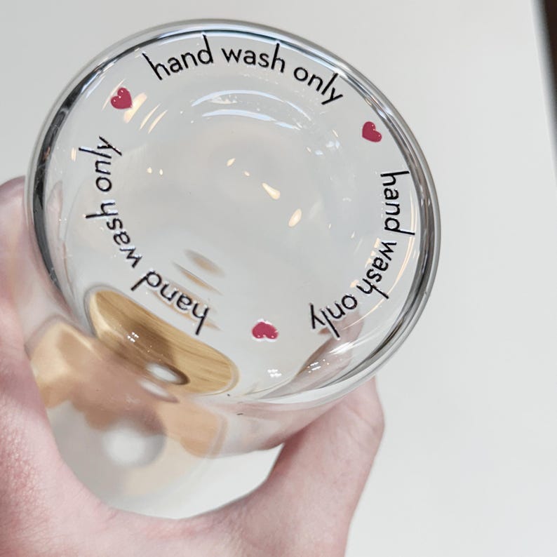 May include: A clear glass cup with a brown wooden handle. The cup has the text "hand wash only" written around the rim with a small red heart on each side.