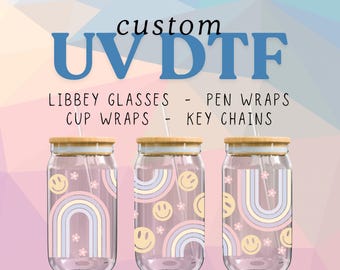 May include: Three clear glass jars with bamboo lids and straws. Each jar features a pink, white and blue rainbow design with smiley faces and small flowers. The jars are labelled "custom UV DTF LIBBEY GLASSES - PEN WRAPS CUP WRAPS - KEYCHAINS"