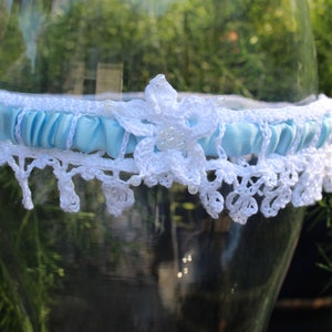 May include: A white crocheted garter with a light blue satin ribbon and a white flower accent.