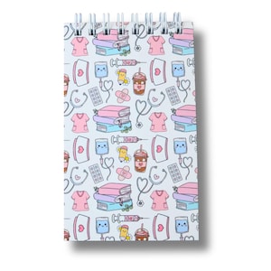 May include: A spiral-bound notepad featuring a repeating pattern of medical illustrations. The design includes pink scrubs, stethoscopes, books, IV drips, syringes, bandages, and coffee cups. The notepad is white with a shadow.