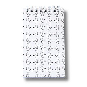 May include: A white, spiral-bound notepad featuring a repeating pattern of black stethoscopes. The medical-themed notebook has a shadow on the right side. The top of the notepad has a silver spiral binding. The notepad is likely for taking notes.