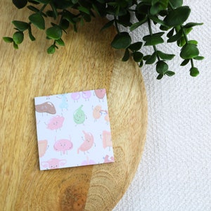 Peut inclure: Une carte blanche avec un motif coloré d'organes de dessin animé. Les organes sont dessinés avec des visages souriants et ont différentes couleurs, notamment le rose, le vert, le marron et le bleu.