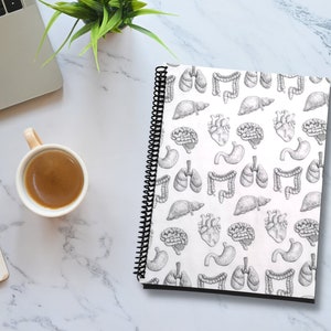 May include: A white spiral bound notebook with a black and white anatomical illustration pattern of the human organs, including the heart, lungs, brain, stomach, and intestines.