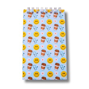 Peut inclure: Un bloc-notes à spirales avec un fond bleu clair. Le bloc-notes présente un motif répété de tasses à café, de stéthoscopes, de visages souriants et de petites fleurs blanches. Les tasses à café portent l'inscription "Coffee".