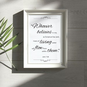 May include: A framed print with the quote "Whoever believes in me, as Scripture has said, rivers of living water will flow from within them." The frame is white, and a green leaf is on the left.