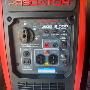 May include: A red and black Predator generator with the brand name in red lettering. The generator has a control panel with various switches, outlets, and indicators, including "1,600 Running Watts" and "2,000 Peak Watts".