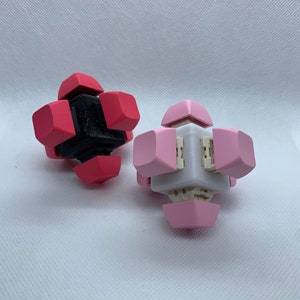 May include: Two small, cube-shaped puzzles. One is pink and the other is red with a black center. Both have a white center piece.