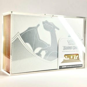 May include: A white and silver Pokemon Sword & Shield Ultra Premium Collection box, featuring a Charizard illustration. The box is encased in a clear acrylic display case.