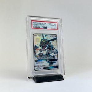 May include: A graded Pok&eacute;mon card featuring Rayquaza GX, encased in a clear protective holder. The card is displayed on a black stand. The label reads "2018 POKEMON SUN & MOON #177b FA/RAYQUAZA GX". The card is graded GEM MT 10.