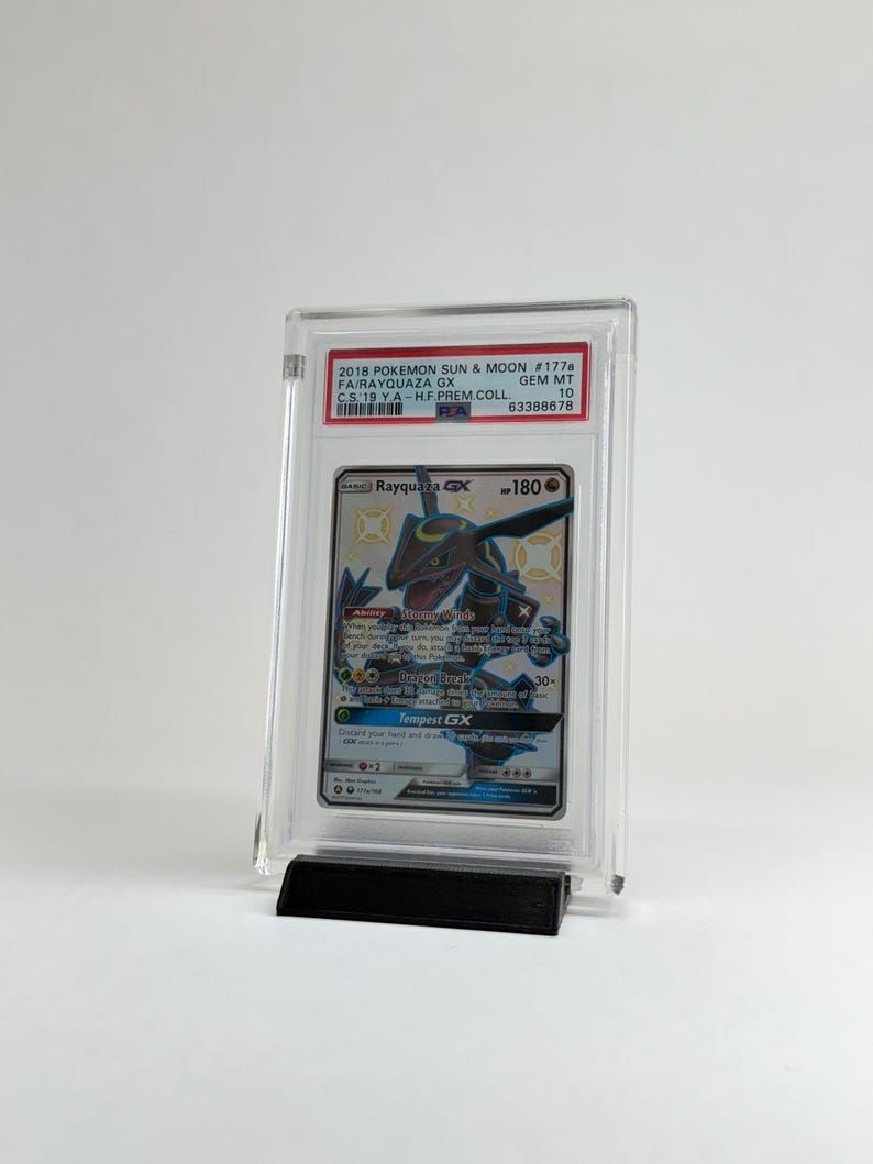 May include: A graded Pok&eacute;mon card featuring Rayquaza GX, from the 2018 Sun & Moon set. The card is encased in a clear protective holder and displayed on a black stand. The card's details include the set number, a grade of 10, and the text "Tempest GX".