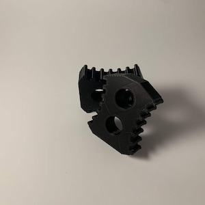 Puede incluir: Dos engranajes de plástico negro con un borde dentado. Los engranajes están entrelazados y tienen un agujero circular en el centro.