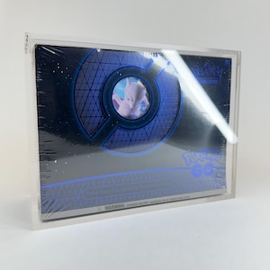 Puede incluir: Una caja de entrenador de élite Pokemon Center sellada en una funda de acrílico transparente. La caja tiene un diseño azul y negro con el logotipo de Pokemon GO y un gráfico de Mewtwo. La caja está envuelta en plástico.