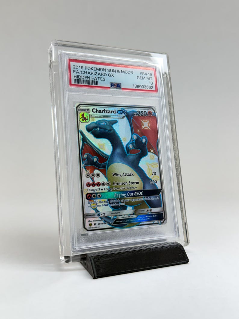 May include: A graded Charizard GX trading card from the 2019 Pokemon Sun & Moon Hidden Fates set. The card is encased in a clear plastic holder and displayed on a black stand. The card features a blue Charizard with red and orange accents.