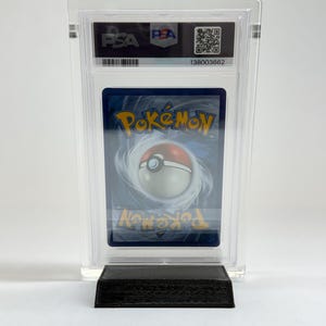 May include: A graded Pok&eacute;mon trading card in a clear plastic case. The card features a blue background with a white and red Pok&eacute;ball design. The case has a PSA label with a QR code and serial number.